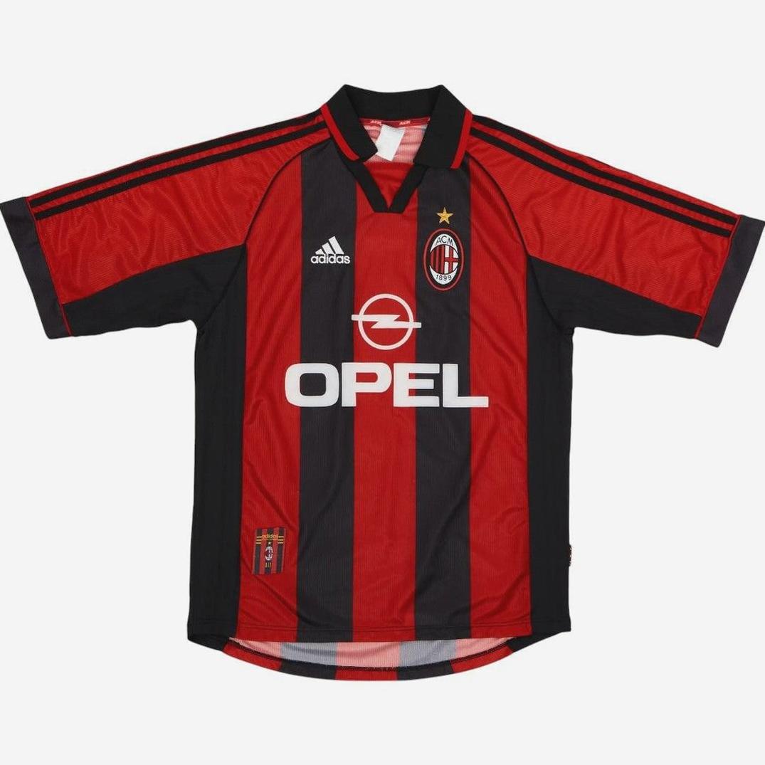 The AC Milan 1998-00 Home Shirt by Retro1999 features red and black stripes, black sleeves, the Adidas logo, Opel sponsor, club badge with a gold star—an iconic retro kit from Serie A football history.