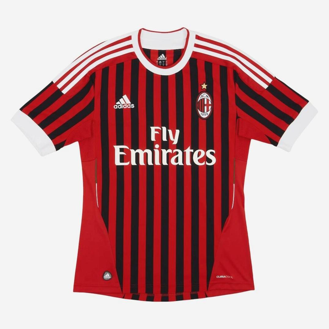 The AC Milan 2011-12 Home Shirt by Retro1999 features red and black stripes, white Adidas shoulder stripes, Fly Emirates sponsor logo, AC Milan badge with gold star—a classic retro kit for Italian football fans.