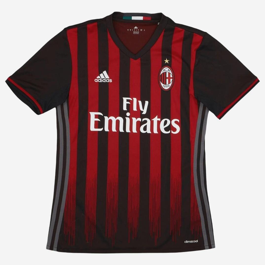 The AC Milan 2016-17 Home Shirt by Retro1999 features classic black and red stripes, short sleeves, V-neck collar, club crest, and sponsor logo. Inspired by iconic Serie A kits for a true retro look.