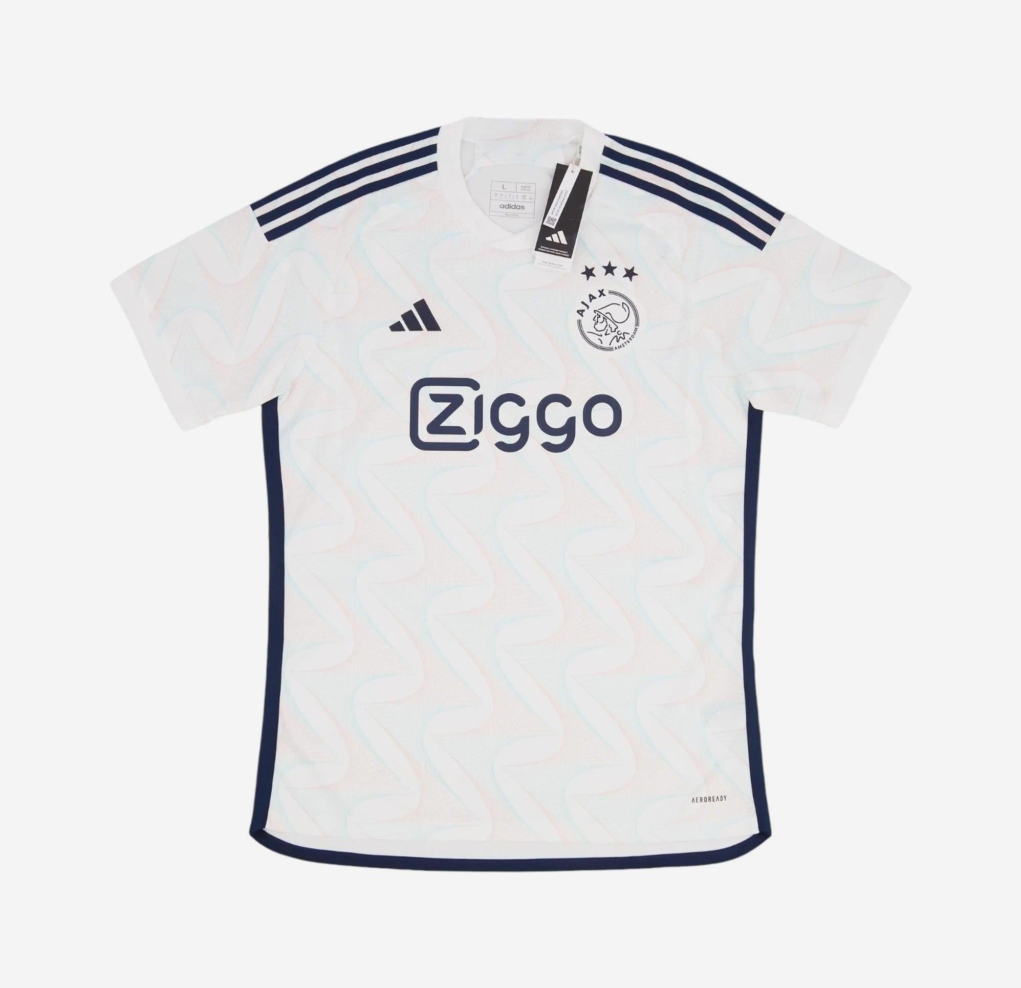The Ajax 2023-24 Away Shirt by Retro1999 features a white base, navy zigzag patterns, navy Adidas shoulder stripes, the Ajax logo with three stars, and Ziggo sponsor logo. Made from premium materials; tag attached at the collar.