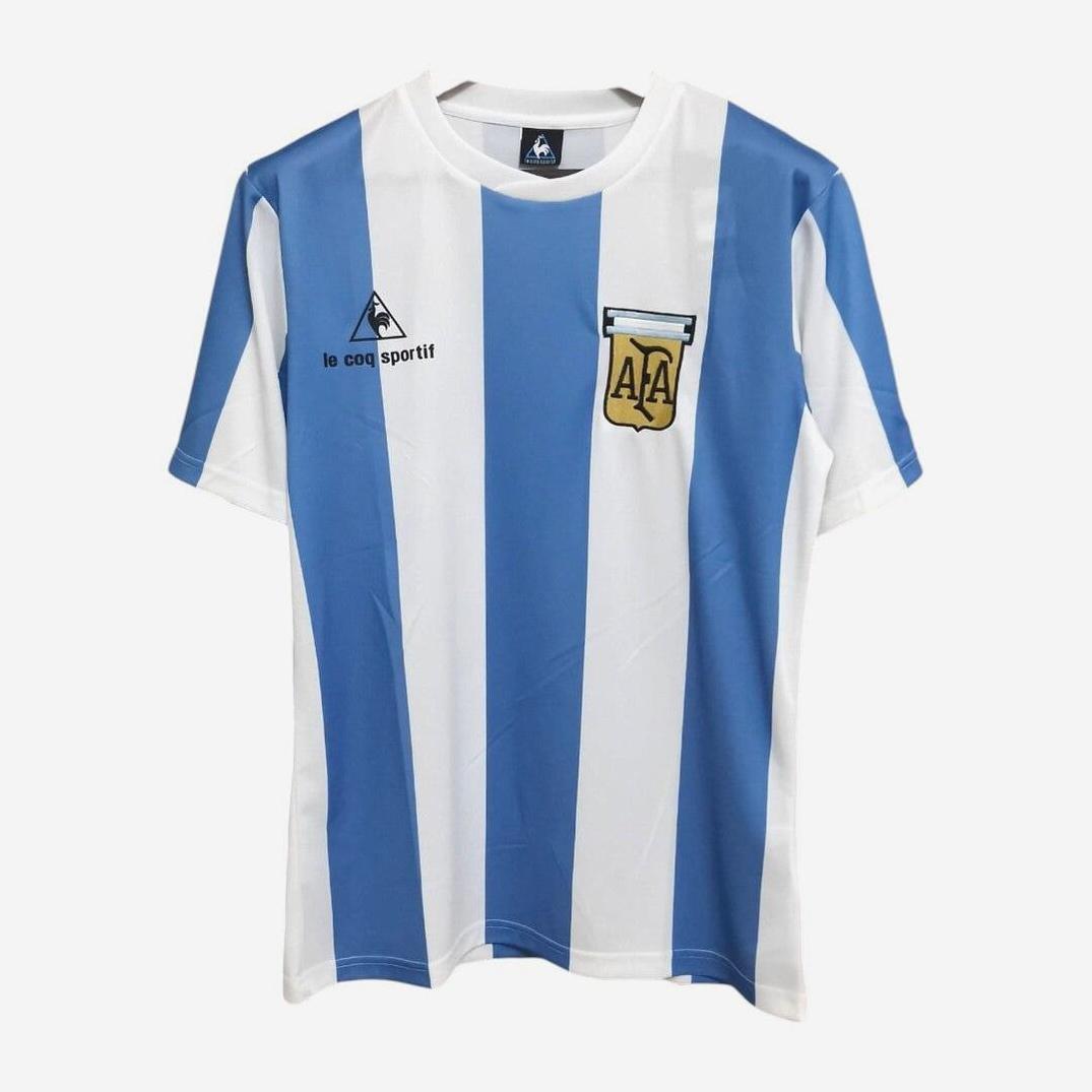 The Retro1999 Argentina 1985 Home Shirt is a short-sleeved jersey with vertical light blue and white stripes, featuring a Le Coq Sportif logo on the right chest and an AFA crest on the left, inspired by the classic retro kit.