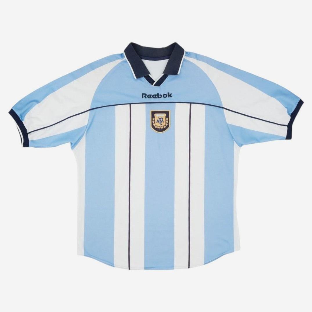 The Retro1999 Argentina 2000/01 Home Shirt features light blue and white stripes, a black collar, the Argentina crest, and Retro1999 logo—a classic short-sleeve retro soccer jersey inspired by the iconic 2000/01 kit.