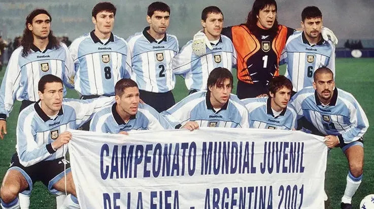 A group of players in Argentina 2000/01 Home Shirts by Retro1999 pose on the field, holding a banner that says: Campeonato Mundial Juvenil de la FIFA - Argentina 2001.