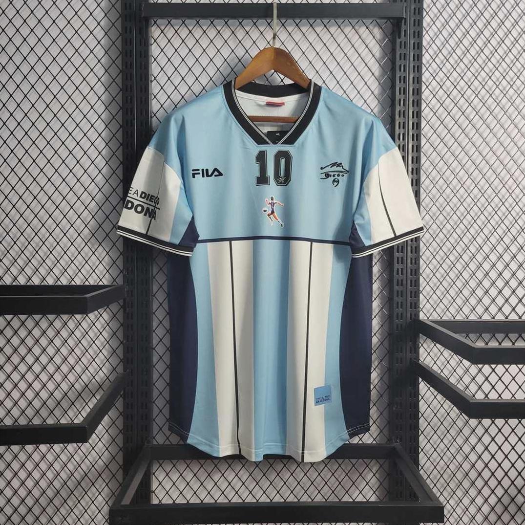 The Argentina 2001 Maradona Commemorative Edition by Retro1999 is a light blue and white striped soccer jersey with black trim, number 10, Fila logo, graphics, and sponsor logos—perfect for football memorabilia collectors.