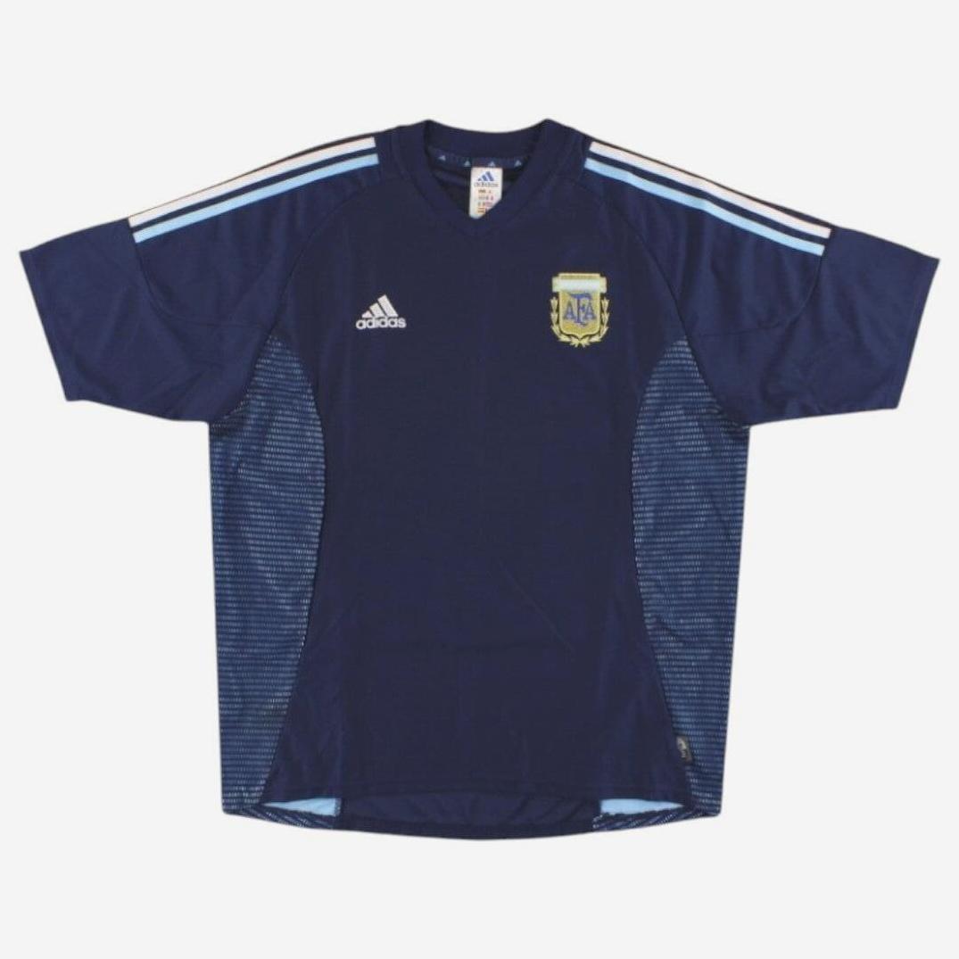 The Argentina 2002 Away Shirt by Retro1999 is dark blue with light blue and white shoulder stripes, an Adidas logo on the right chest, and the national team crest—an iconic retro piece.