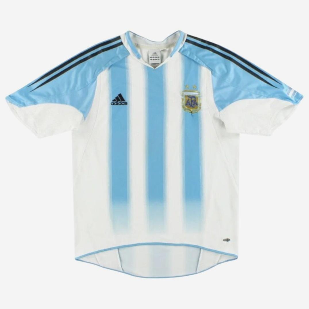 The Argentina 2004-05 Home Shirt by Retro1999 features classic white and light blue stripes, black adidas-style details on the shoulders, and the Argentine Football Association crest—a timeless nod to football heritage.