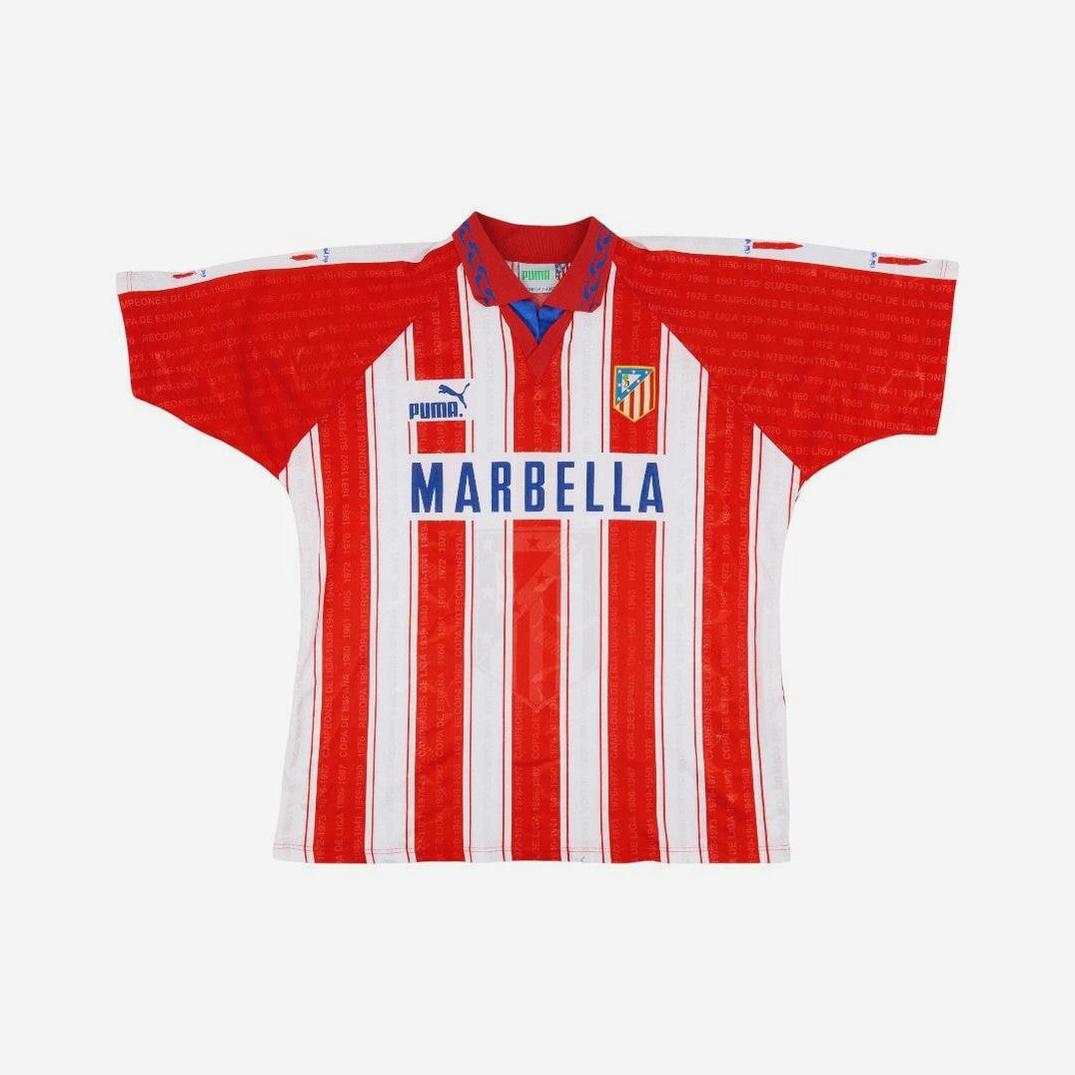 The Retro1999 Atletico Madrid 1995-96 Home Shirt features red and white vertical stripes, a blue collar, Puma logo, club crest, and Marbella sponsor—a classic design honoring a golden era in La Liga history.