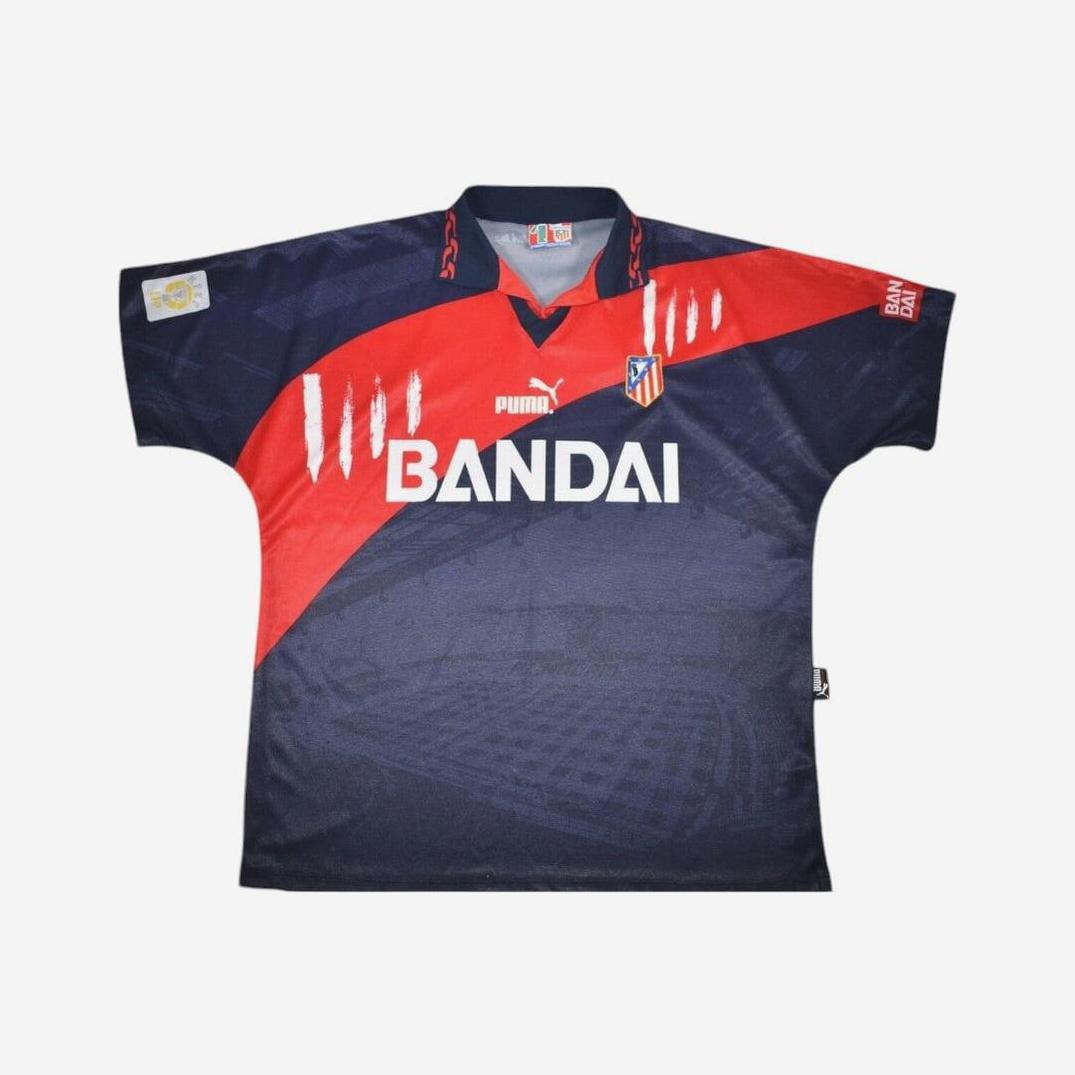 The Atletico Madrid 1996-97 Away Shirt by Retro1999 is a dark blue retro kit with red diagonal stripes, club crest, and classic logos, shown on a plain white background.
