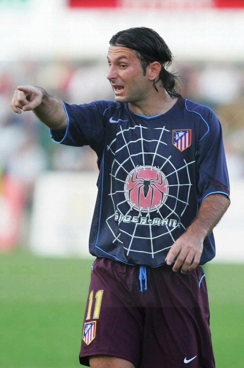 A soccer player on the field wears a Retro1999 Atletico Madrid 2004-05 Away Shirt in dark blue with a large Spider-Man logo, pointing and gesturing during a match.