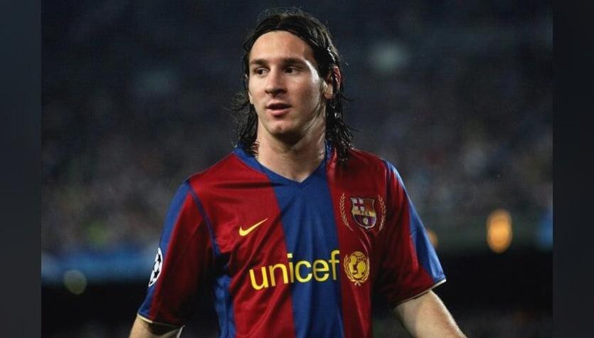 A male soccer player wears the Retro1999 Barcelona 2007-08 Home Shirt featuring Unicef on the front, standing on the field during a match with a blurred crowd in the background, recalling the Frank Rijkaard era.