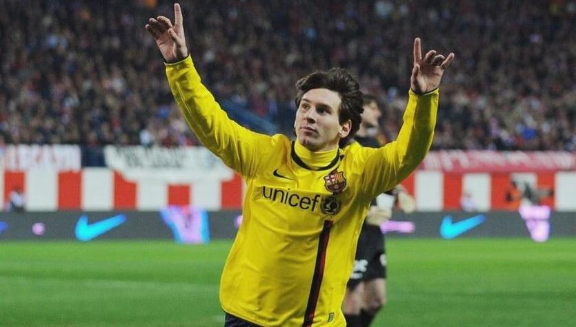 A soccer player celebrates on the field in a Retro1999 Barcelona 2008-09 Away Shirt, with arms raised. The crowd and stadium advertising boards highlight the shirt’s authentic retro style.