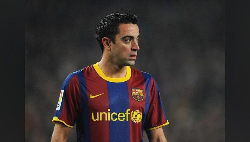 A soccer player in the Retro1999 Barcelona 2010-11 Home Shirt with red and blue stripes and unicef on the front stands on the field with an armband, gazing sideways—the blurred background adds to this classic football scene.