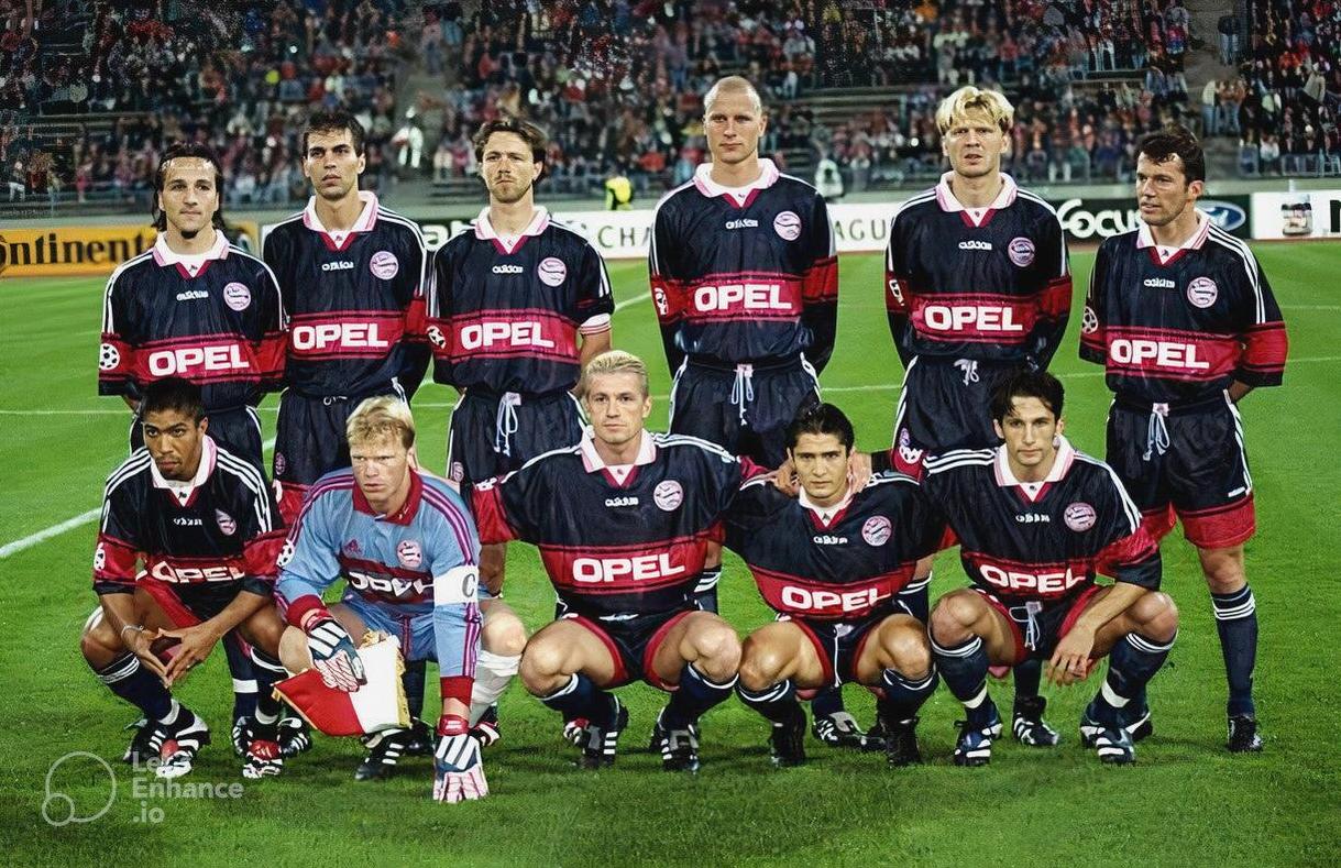 A soccer team wearing the Retro1999 Bayern Munich 1997-98 Away Shirt with Opel sponsor poses on the field—five players stand, six kneel. A packed stadium background makes this a true piece of Bundesliga memorabilia.
