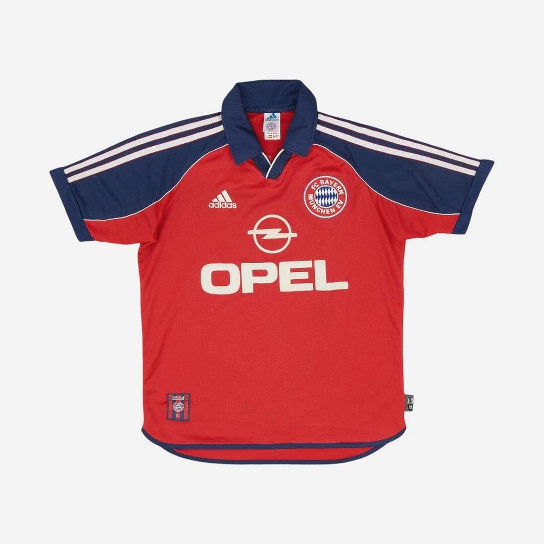 The Bayern Munich 1999-01 Home Shirt by Retro1999 is a red and navy jersey with classic white adidas stripes, team crest, adidas logo, OPEL sponsor, and commemorates Bayern’s proud Bundesliga heritage.