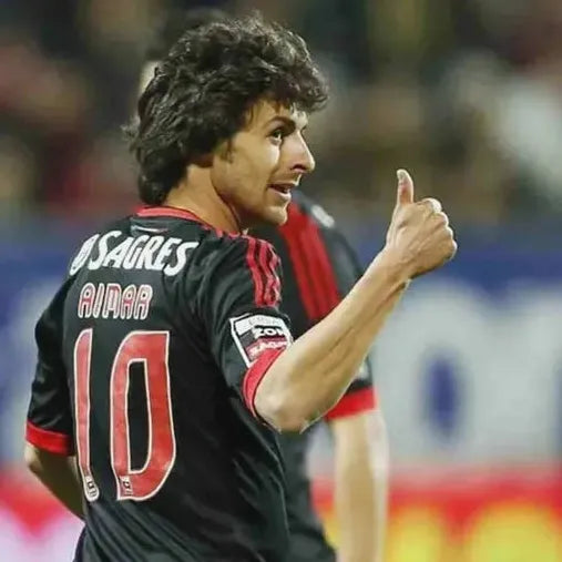 A soccer player wearing the Retro1999 Benfica 2009-10 Away Shirt with Aimar and number 10 gives a thumbs up on the field during a Primeira Liga match.