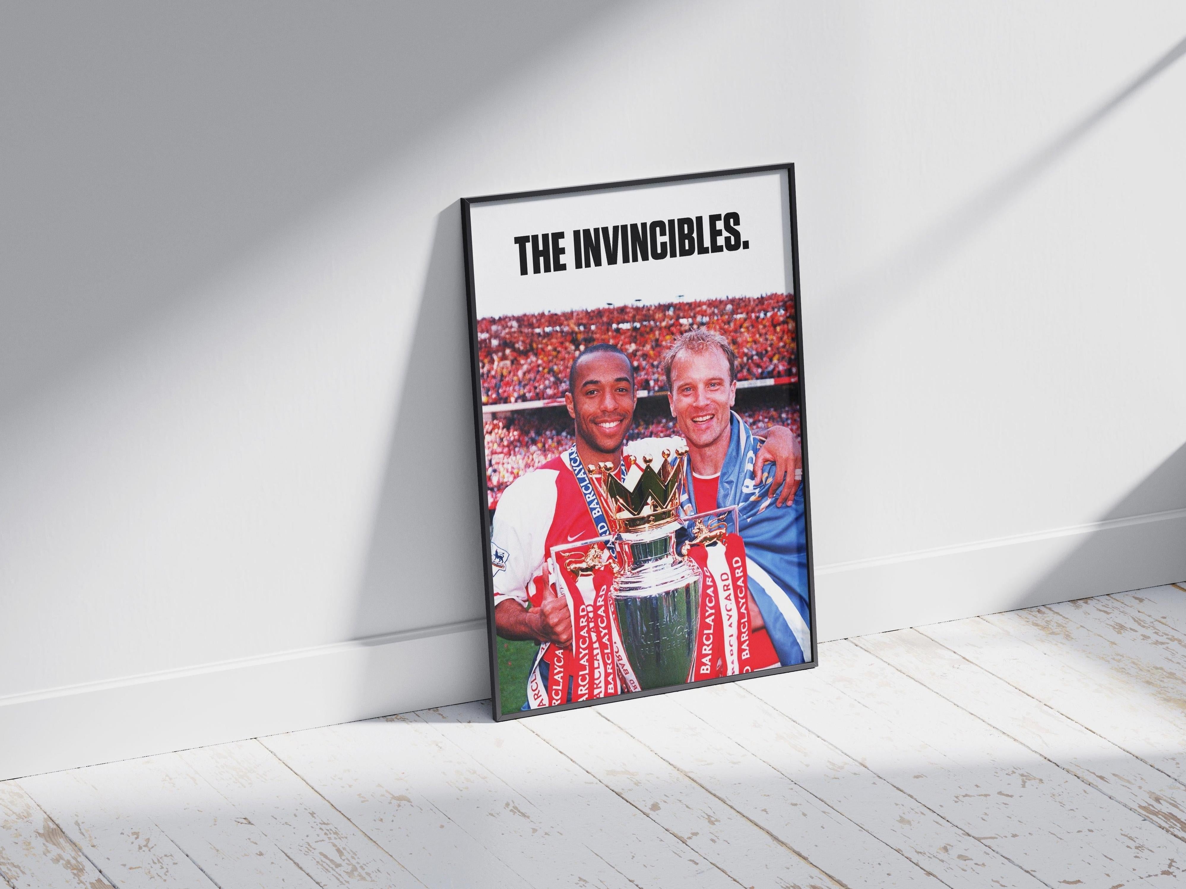 The Bergkamp x Henry The Invincibles Poster by Retro1999 features two smiling Arsenal legends in club kits holding the Premier League Trophy, with “THE INVINCIBLES.” above and cheering fans in the background.