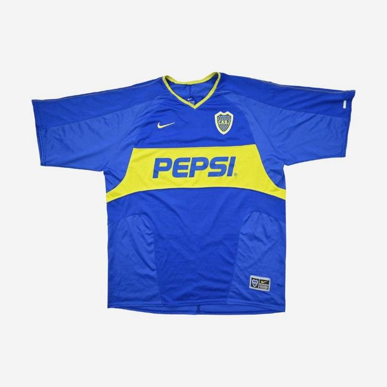 The Boca Juniors 2003-04 Home Shirt by Retro1999 features a blue base with a yellow diagonal band, PEPSI sponsor, Nike logo, and club badge—an iconic retro kit from the 2004 Copa Sudamericana.