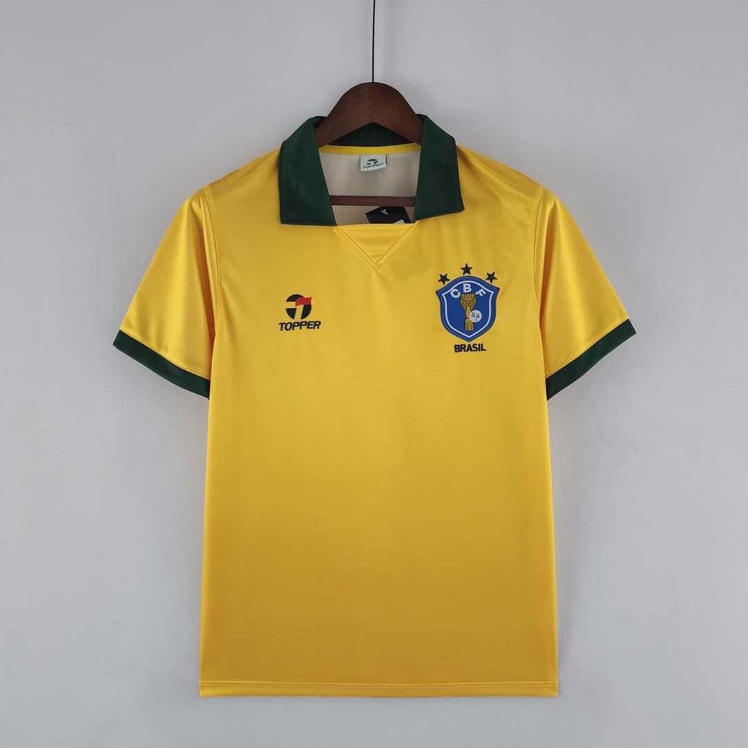 A yellow Brazil 1988 Home Shirt by Retro1999 with green collar and sleeve edges hangs on a wooden hanger, featuring the team crest and celebrating classic Brazilian football style.
