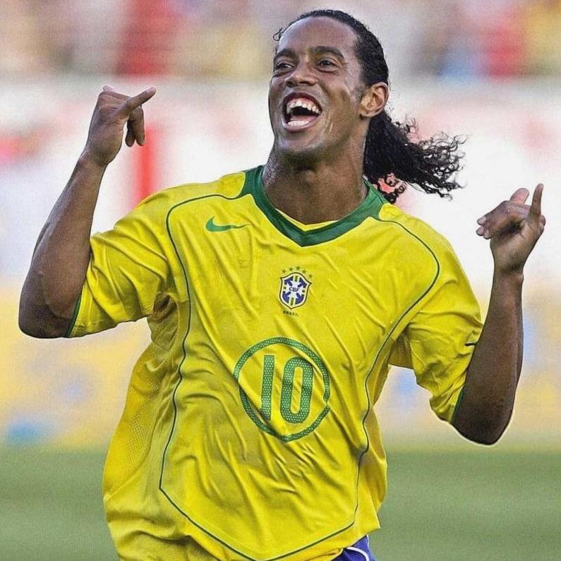 A Brazilian soccer player in a yellow Retro1999 Brazil 2004 Home Shirt with number 10 celebrates joyfully on the field, smiling with arms raised and hair tied back, embodying classic Brazilian football spirit.