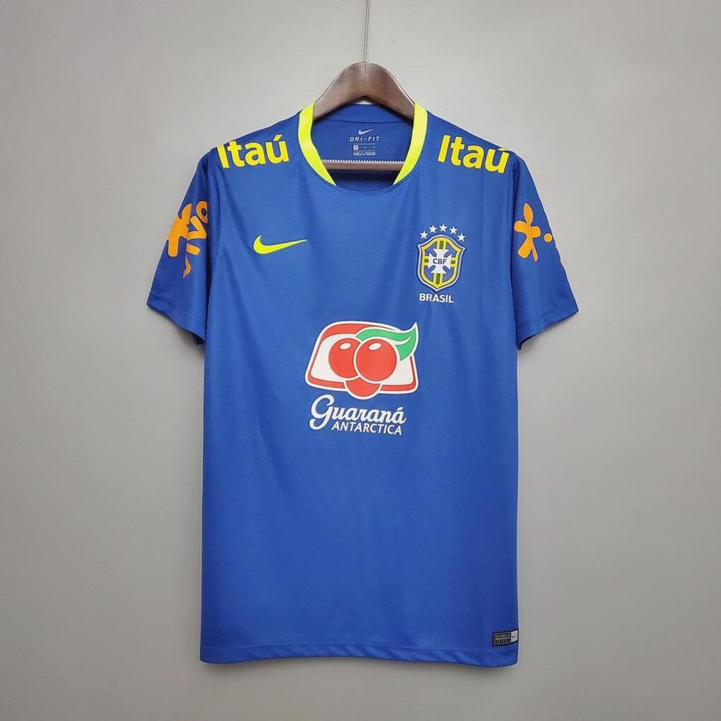 The Brazil 2020 Training Shirt by Retro1999 features blue fabric with yellow accents, team crest, and sponsor logos, crafted from breathable material and shown on a hanger against a plain gray wall.