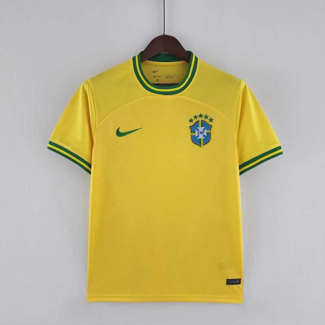 The Brazil 2022 Home Shirt by Retro1999 features yellow fabric with green collar and sleeve trim, plus the national crest with five stars and a Nike logo—offering a classic retro kit look as it hangs on a wooden hanger.