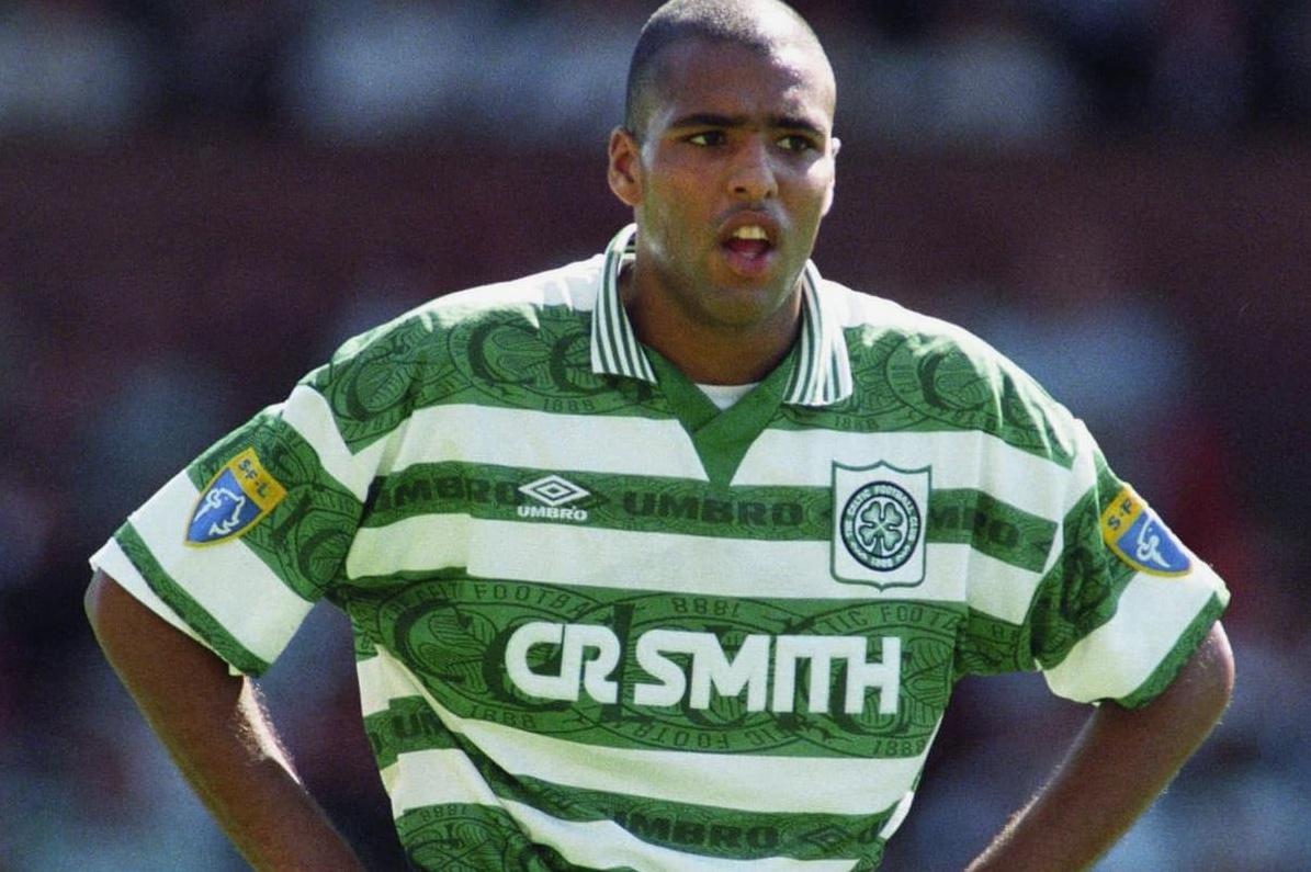 A soccer player in the Retro1999 Celtic 1995-97 Home Shirt with CR SMITH sponsor stands on the field, hands on hips, looking focused—a classic Scottish football moment.