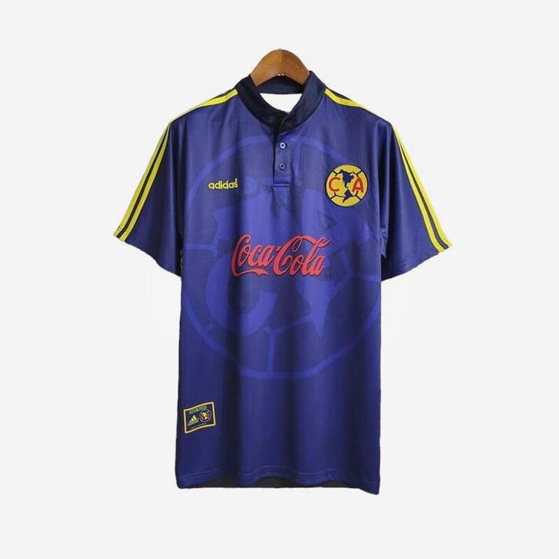 A CF America 1998-99 Away Shirt by Retro1999, blue with yellow Adidas stripes, Coca-Cola sponsor, and team crest on the chest, hangs on a wooden hanger against a white background.