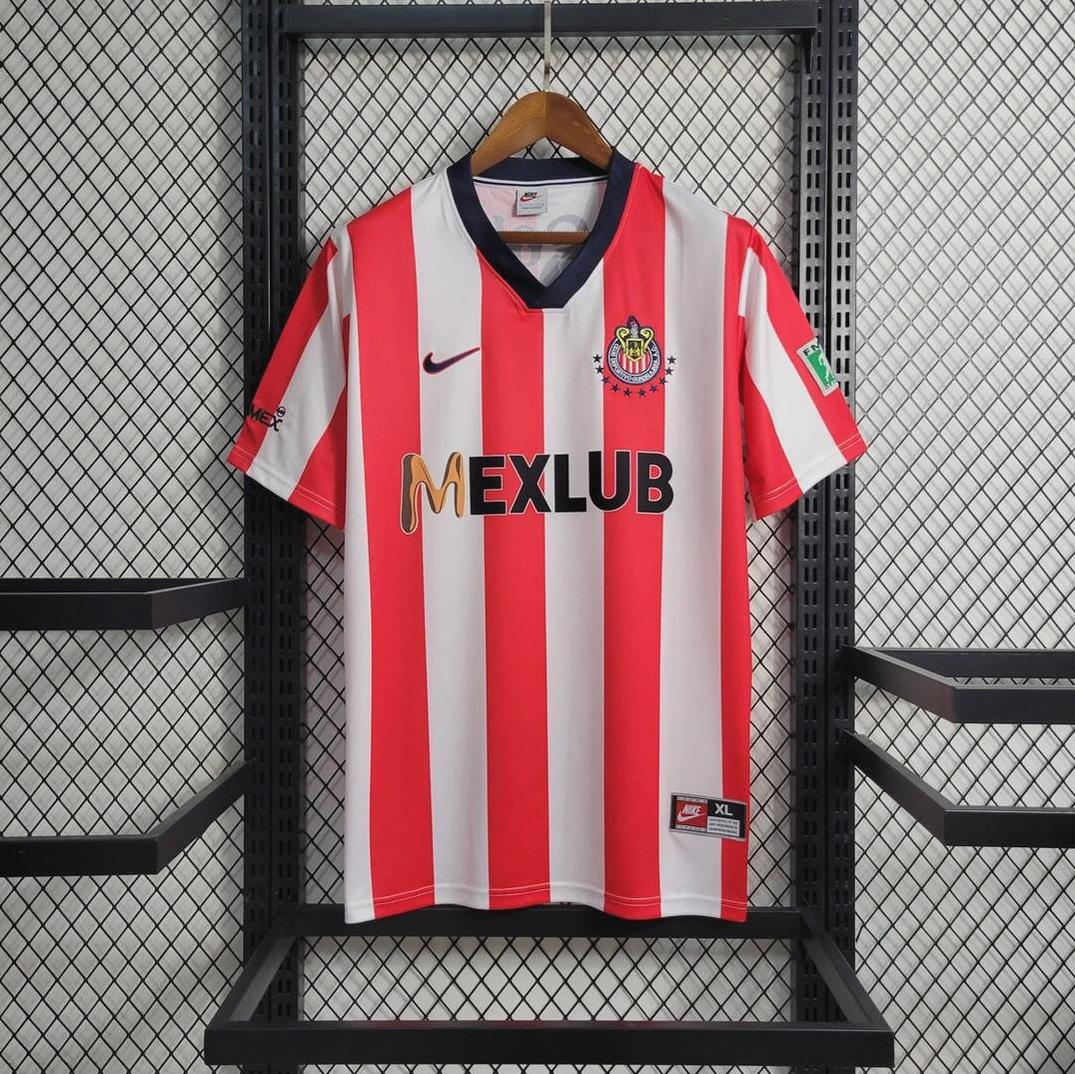 A Chivas 1996-97 Home Shirt by Retro1999, featuring classic red and white stripes, hangs on a black metal rack—ideal for collectors or as a retro kit—displayed against a white textured wall.