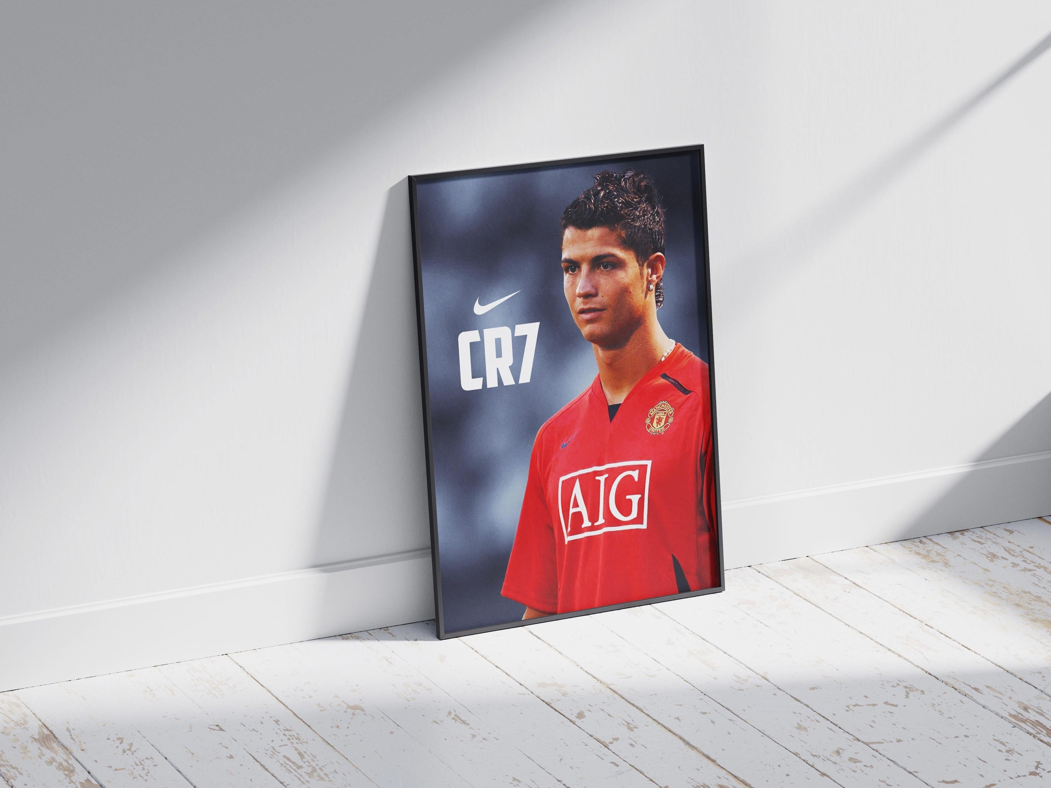 The Retro1999 CR7 Manchester United Poster showcases Cristiano Ronaldo in a red AIG jersey, framed and leaning against a white wall—perfect football memorabilia for any fan.