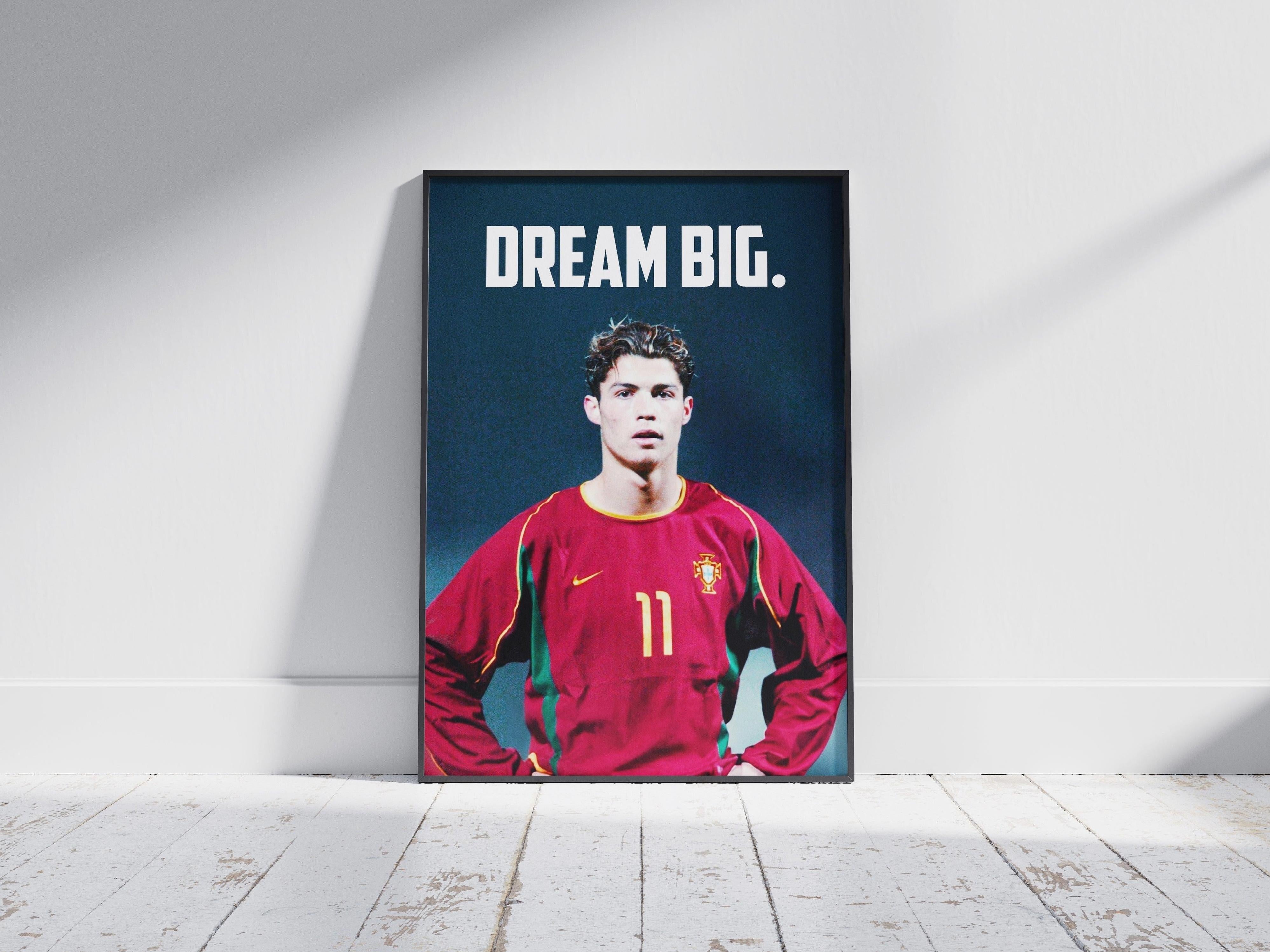 The Retro1999 CR7 x Portugal Poster shows a young soccer player in a red Portugal #11 jersey with DREAM BIG. above him, framed and resting on a white wooden floor—an inspiring piece for football fans. Sunlight brightens the minimalist wall behind.