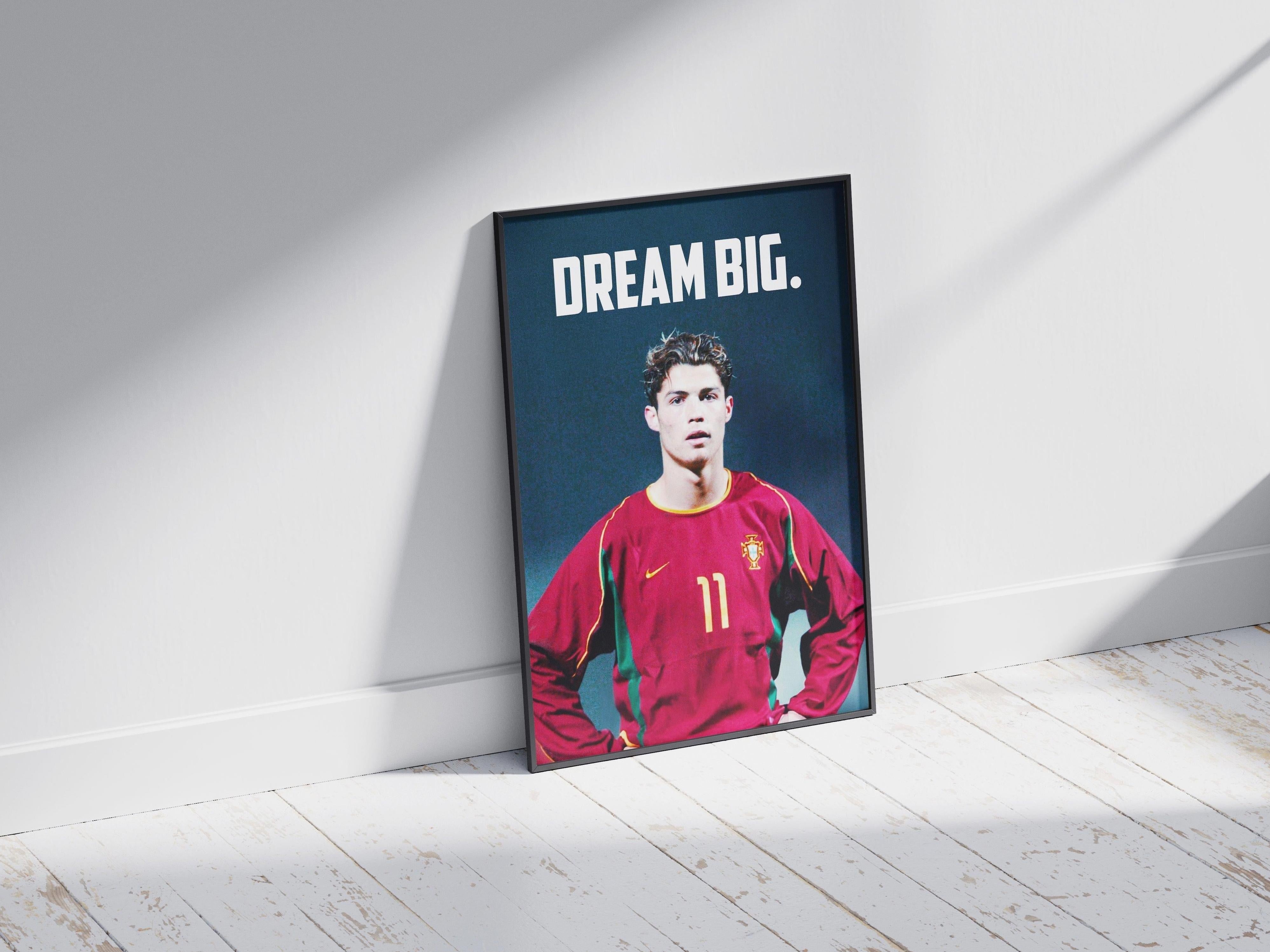 The Retro1999 CR7 x Portugal Poster shows a young male in a red Portugal #11 jersey beneath bold DREAM BIG text, framed and displayed on a sunlit wooden floor—ideal decor for football lovers and Cristiano Ronaldo fans.