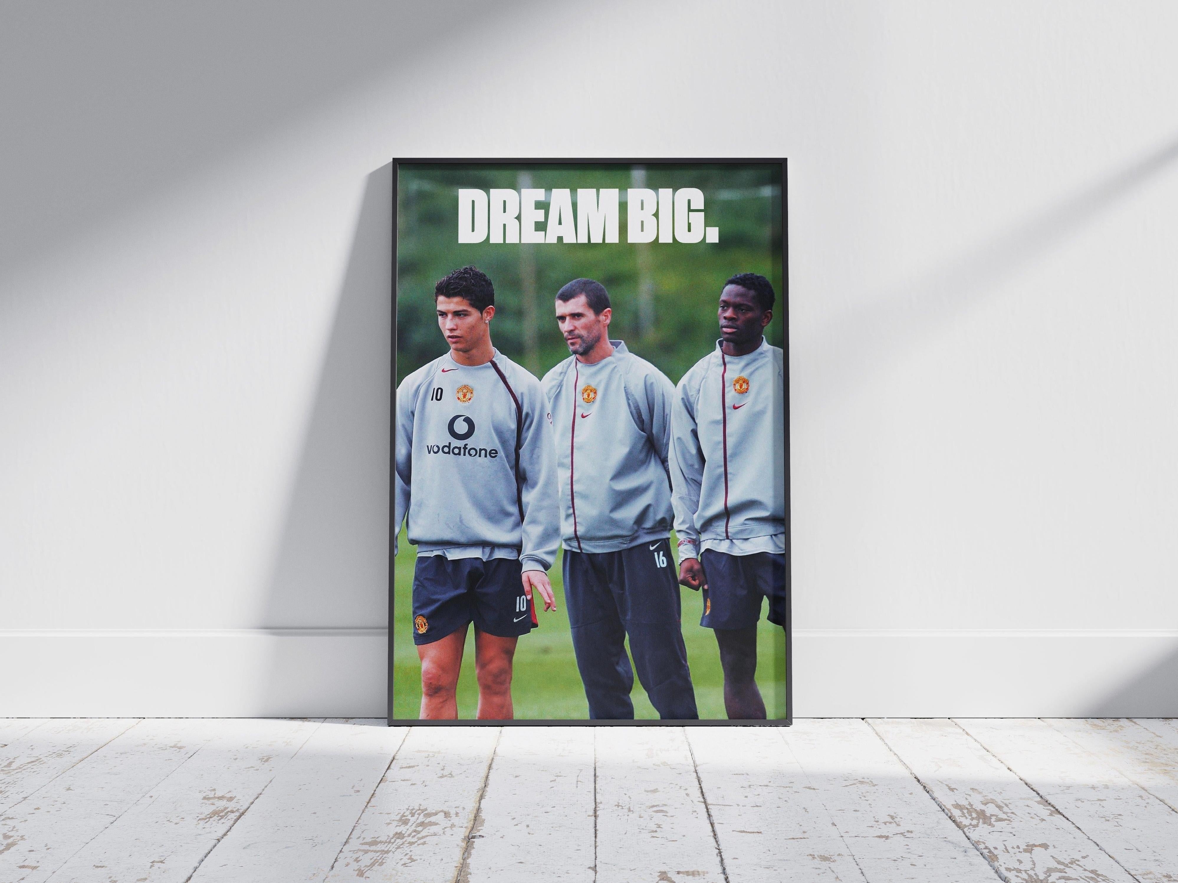 The Retro1999 Cristiano Ronaldo Dream Big Poster features three Manchester United players in training gear with bold “DREAM BIG.” text, framed and placed on a wooden floor—ideal decor for football enthusiasts.