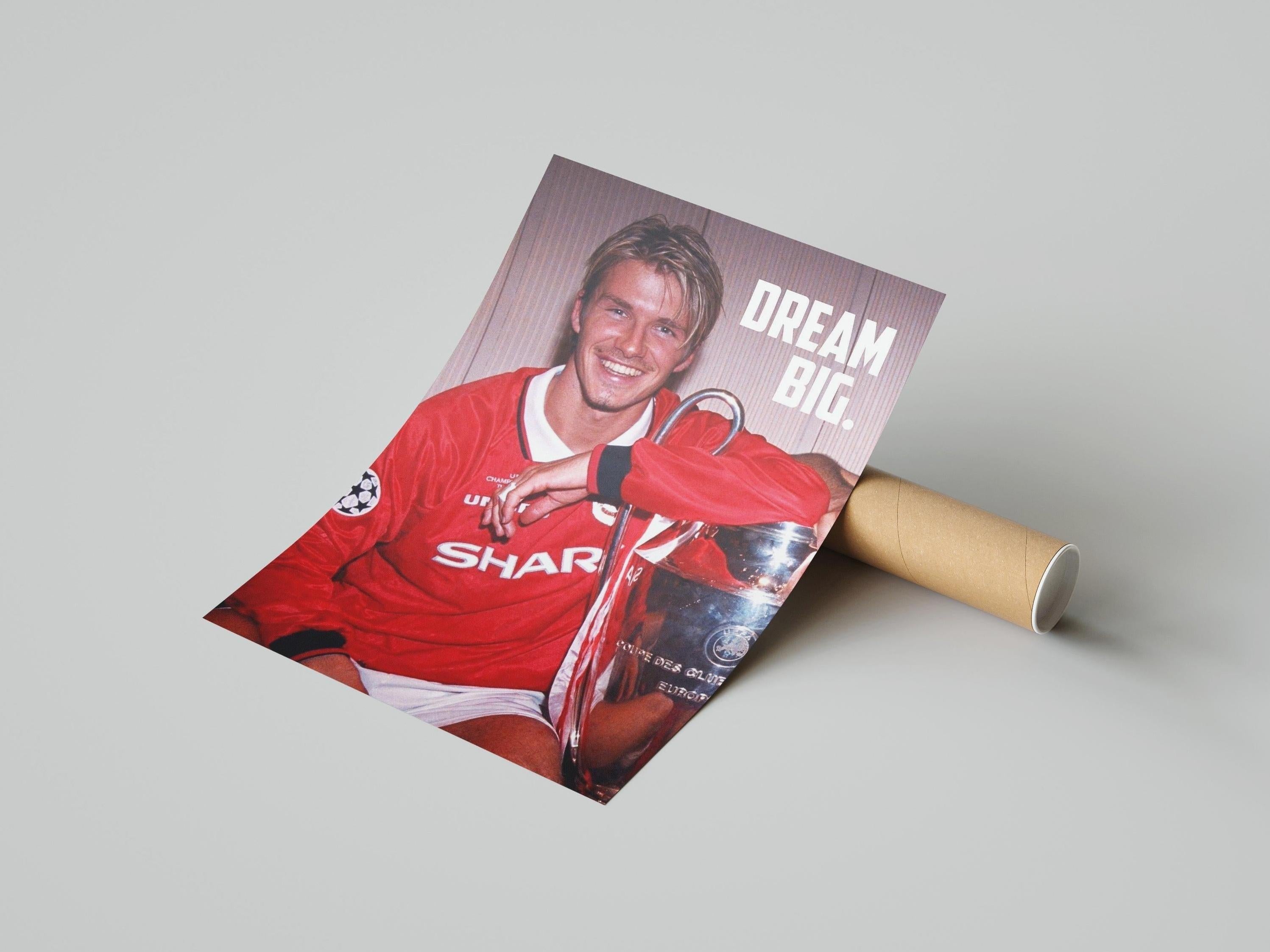 The Retro1999 David Beckham Dream Big Poster features Beckham in a red jersey with a trophy, alongside inspiring text—ideal for UEFA Champions League fans. The poster is partially rolled on a cardboard tube against a plain background.