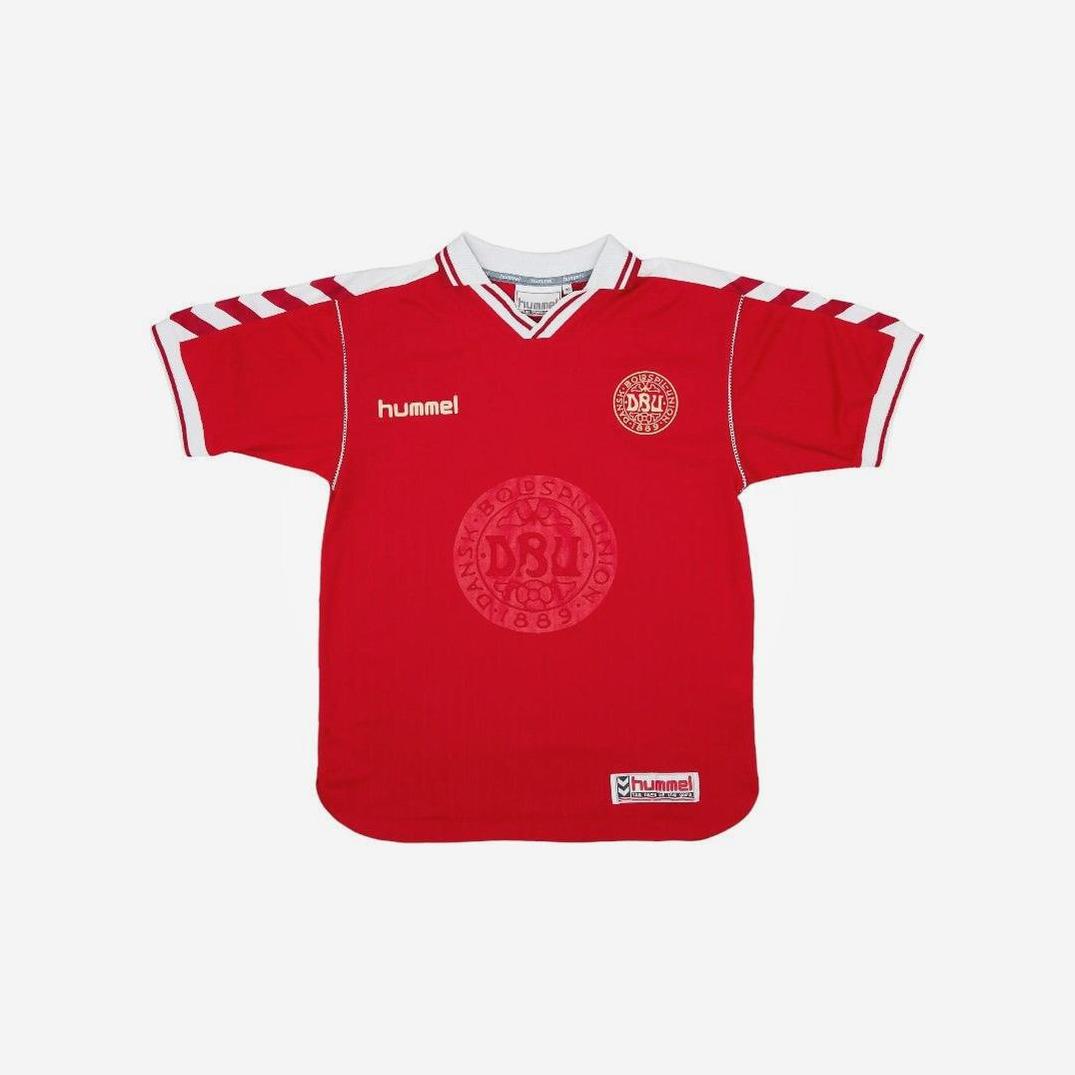 The Retro1999 Denmark 1998 Home Shirt features a red design with white shoulder and collar details, Hummel logo, DBU crest on the left, and a large circular DBU emblem in the center. Set against a plain white background—perfect for football fans.