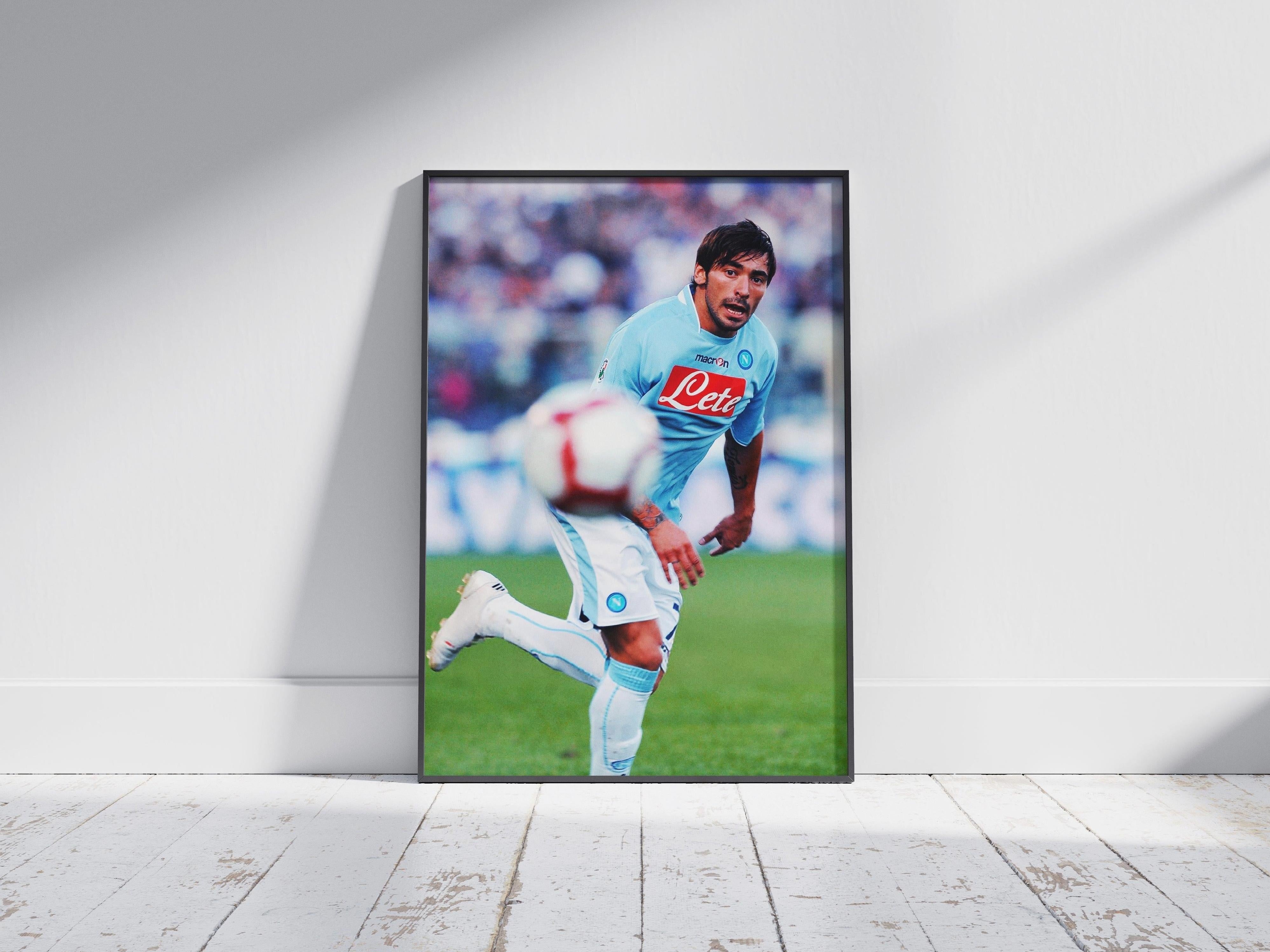 The Retro1999 Ezequiel Lavezzi x SSC Napoli Poster shows Lavezzi in a light blue kit, running on the field during a Serie A match, with a blurred soccer ball in the foreground and leaning against a white wall.