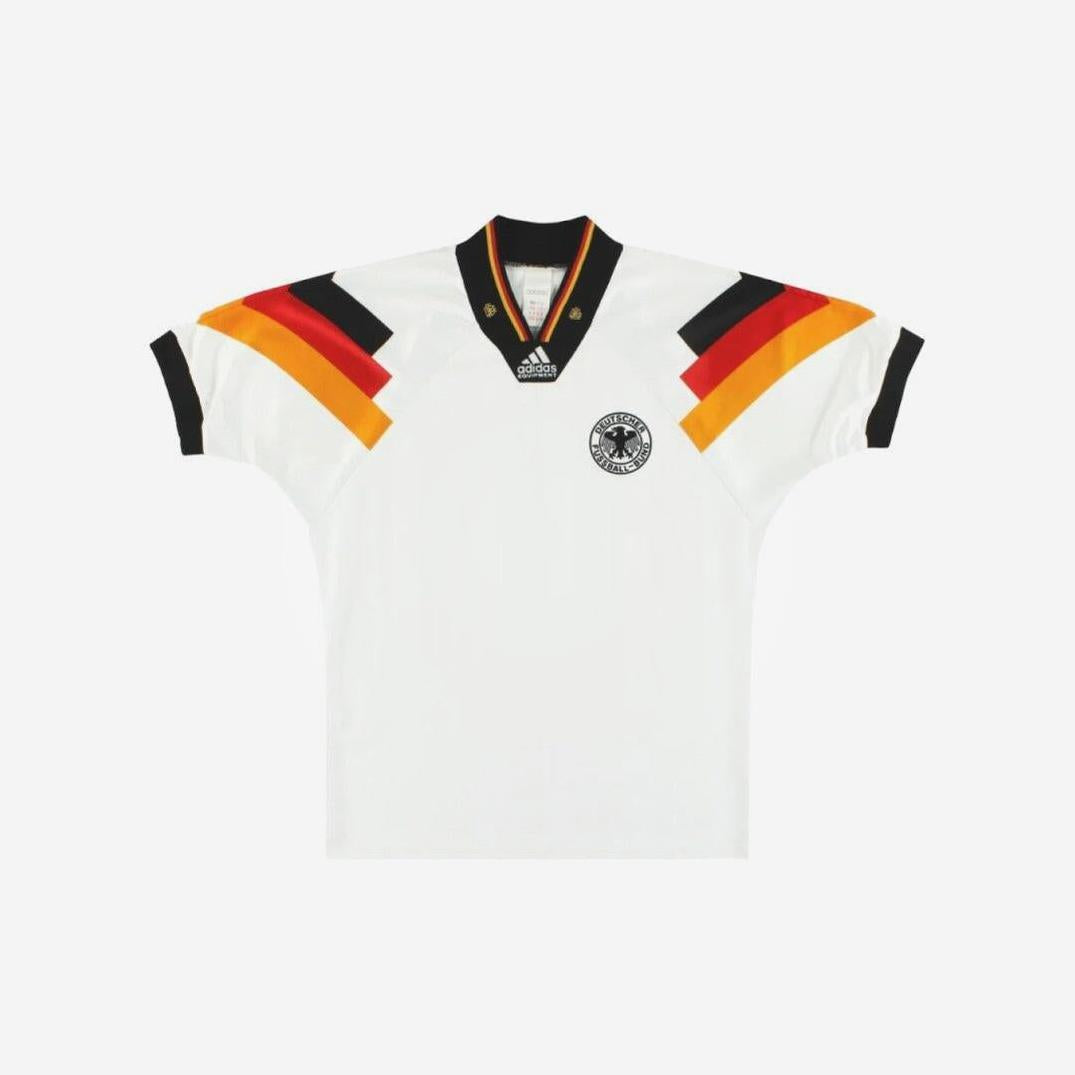 The Retro1999 Germany 1992 Home Shirt is a white football kit with black, red, and yellow sleeve and collar stripes, plus a black eagle badge on the left chest—a must-have retro piece for fans.