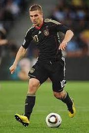 A soccer player in a Retro1999 Germany 2010 Away Shirt with number 10 dribbles a white ball on grass, wearing yellow boots and representing the German national team.