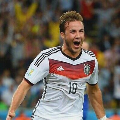 A soccer player celebrates on the field wearing the Retro1999 Germany 2014 Home Shirt, number 19, arms outstretched and mouth open, with a blurred crowd behind highlighting the shirt’s authentic design.