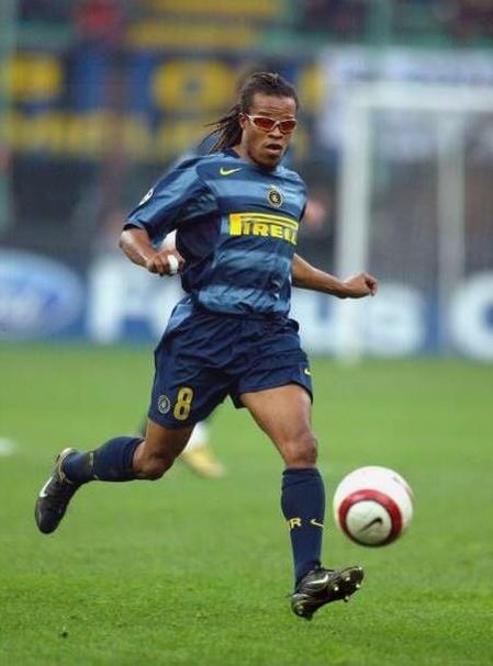 A soccer player wearing a Retro1999 Inter Milan 2004-05 Third Shirt and sunglasses runs on the field, focused on a red and white ball.