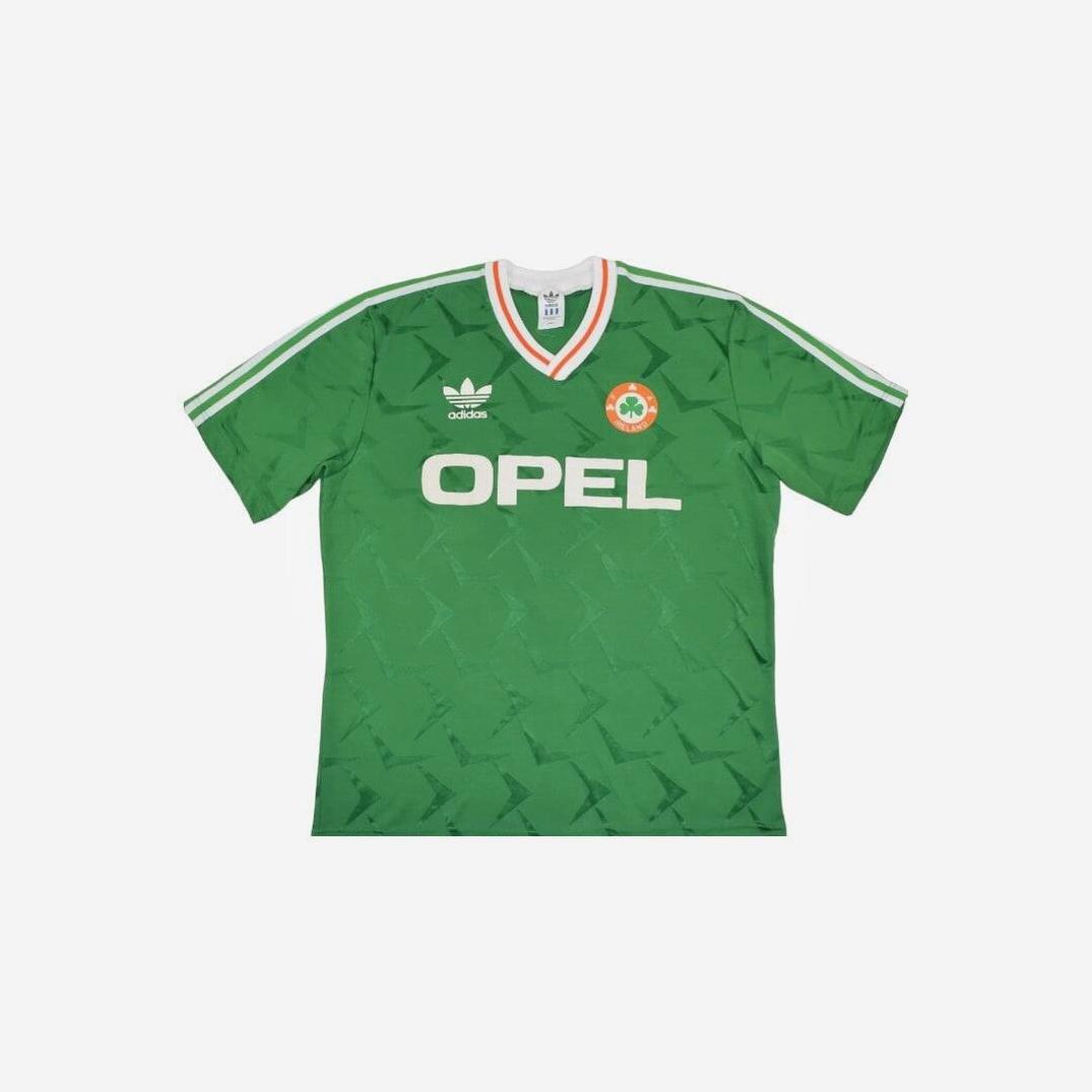 The Retro1999 Ireland 1990 Home Shirt is a green vintage soccer jersey featuring white Adidas-style stripes, classic team logo, Opel sponsor, and orange, white & green V-neck trim—a true retro kit.
