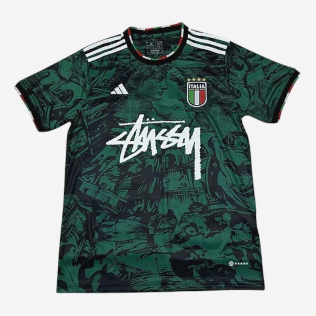 The Retro1999 Italy 2024-25 Away Shirt comes in green and black with an abstract pattern, white shoulder stripes, an Italia badge, and a bold white Stüssy logo—ideal for football fans who value premium materials.