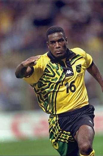 A soccer player wearing the Retro1999 Jamaica 1998 Home Shirt with number 16 and the nations flag sprints across the field, capturing classic Reggae Boyz spirit.