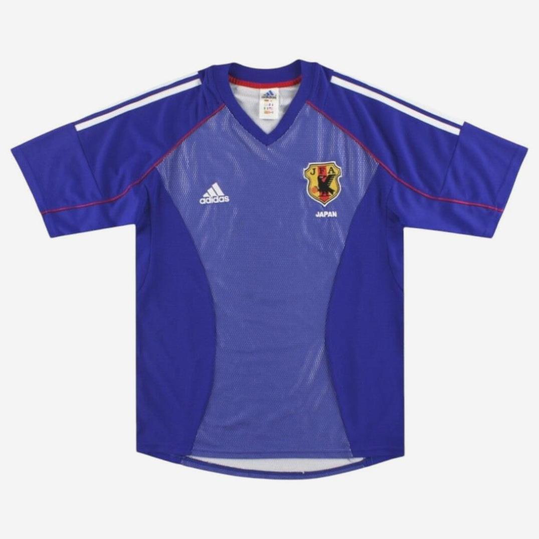 The Japan 2002 Home Shirt by Retro1999 features blue fabric, white shoulder stripes, the Adidas logo on the right chest, and the Japan team crest on the left—ideal for fans of classic national football kits.