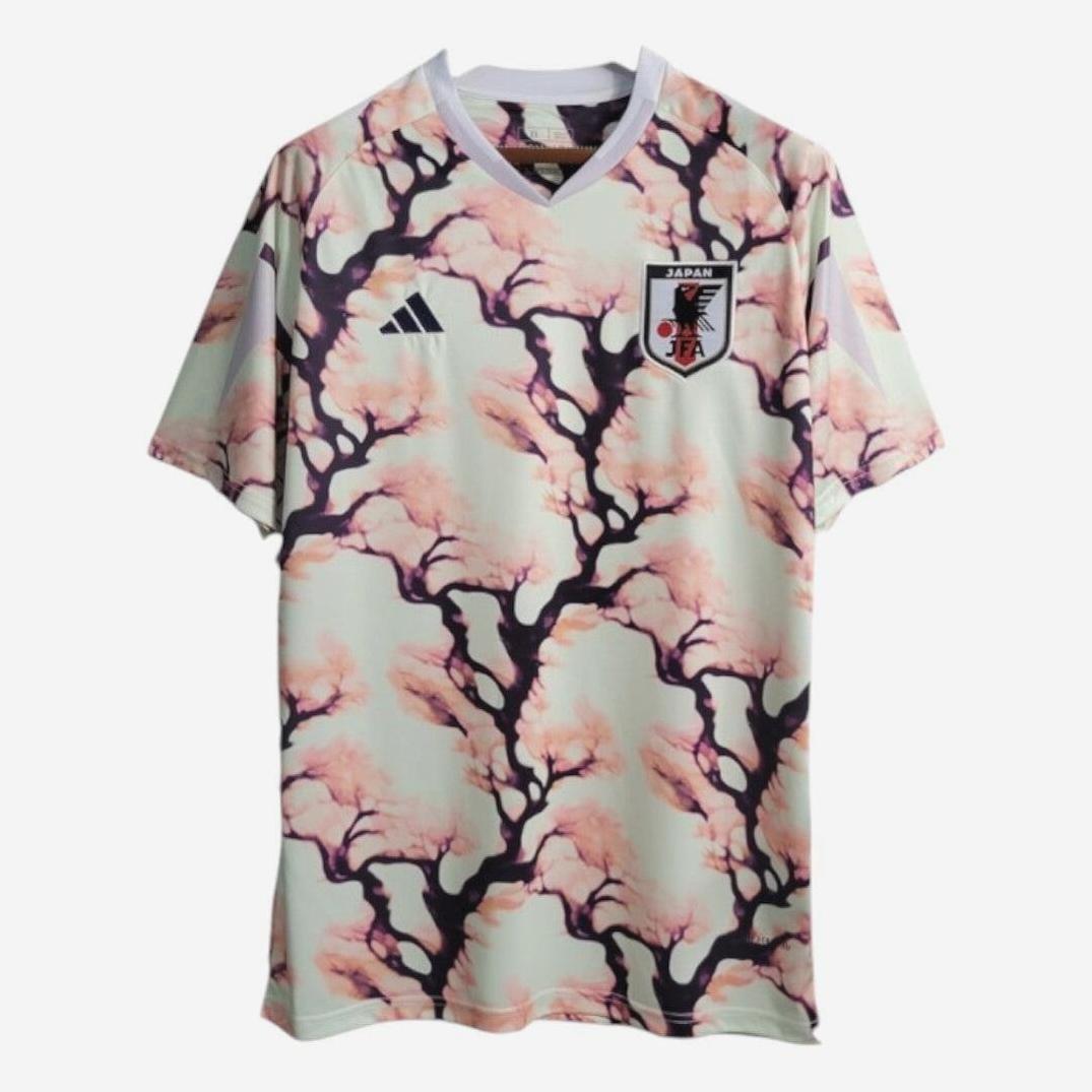 The Japan 2023 Cherry Tree Shirt by Retro1999 is a short-sleeved top with a pink and black cherry blossom design, featuring the Japan National Team crest and Adidas logo for an authentic Japanese style.