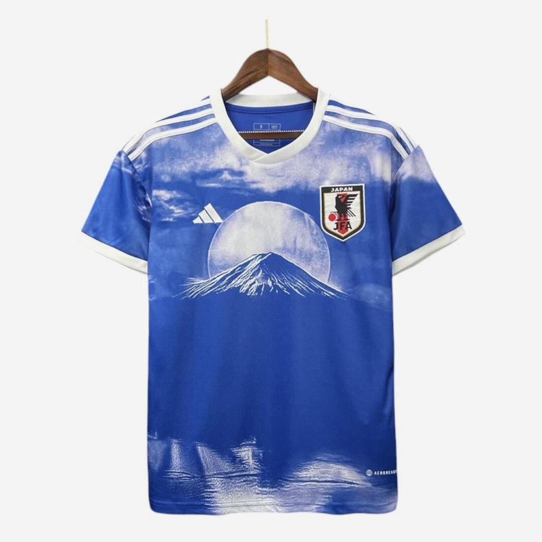 The Japan 2023/24 Mount Fuji Special Edition by Retro1999 is a blue jersey with white shoulder stripes, featuring Mount Fuji and a sun graphic, plus Adidas logo and Japan Football Association crest on the chest.