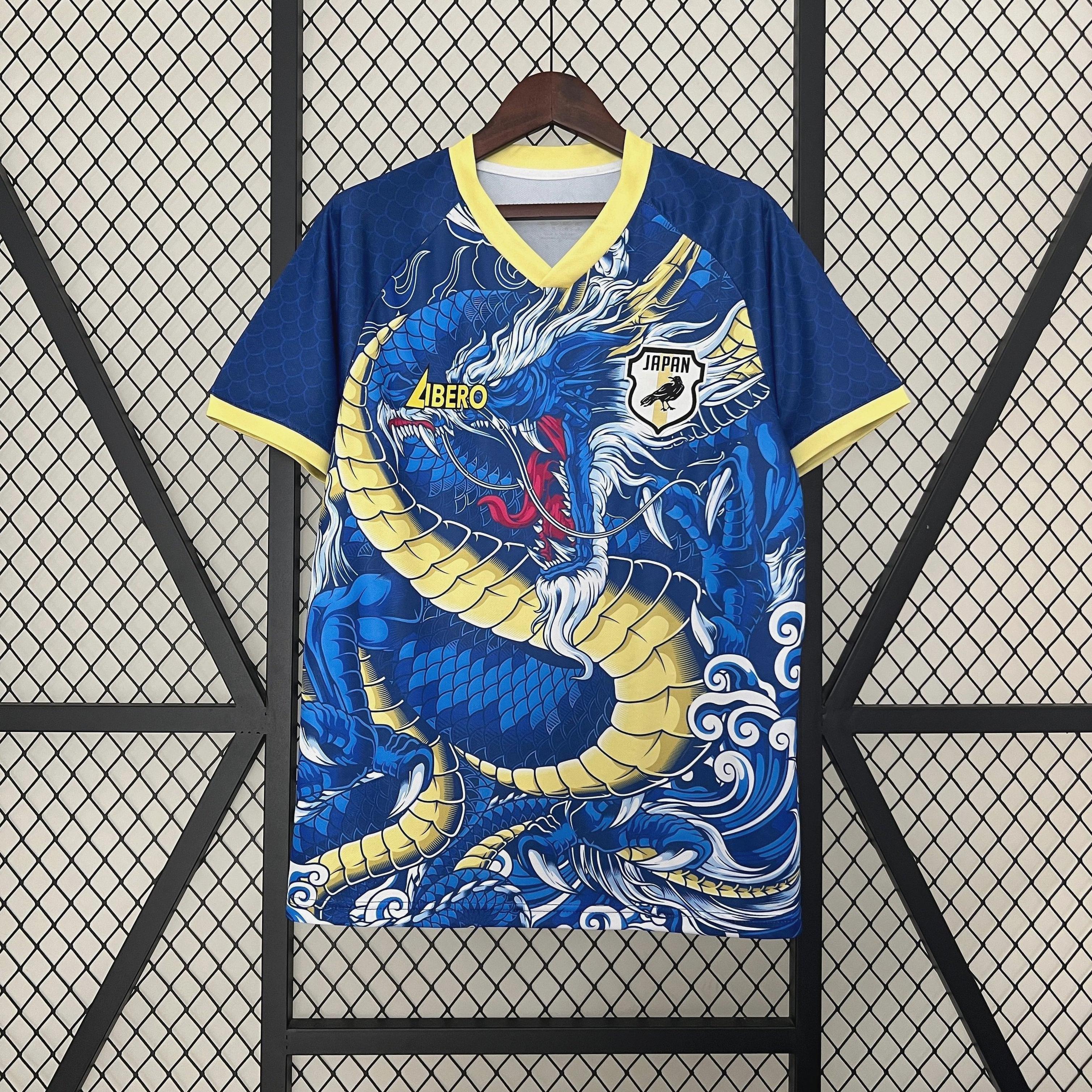 The Retro1999 Japan 2024 Dragon Special Edition sports jersey in blue and yellow hangs on a wooden hanger against a black grid, featuring LIBERO, JAPAN, and wave graphics inspired by classic Japan national team kits.