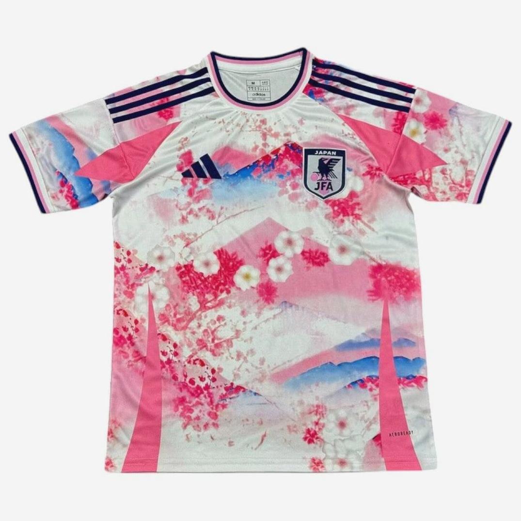 The Retro1999 Japan 2024 Special Edition Shirt showcases a pink, white, and blue design with cherry blossoms, mountain patterns, dark blue shoulder stripes, and the JFA crest—celebrating retro style for the Japan national team.