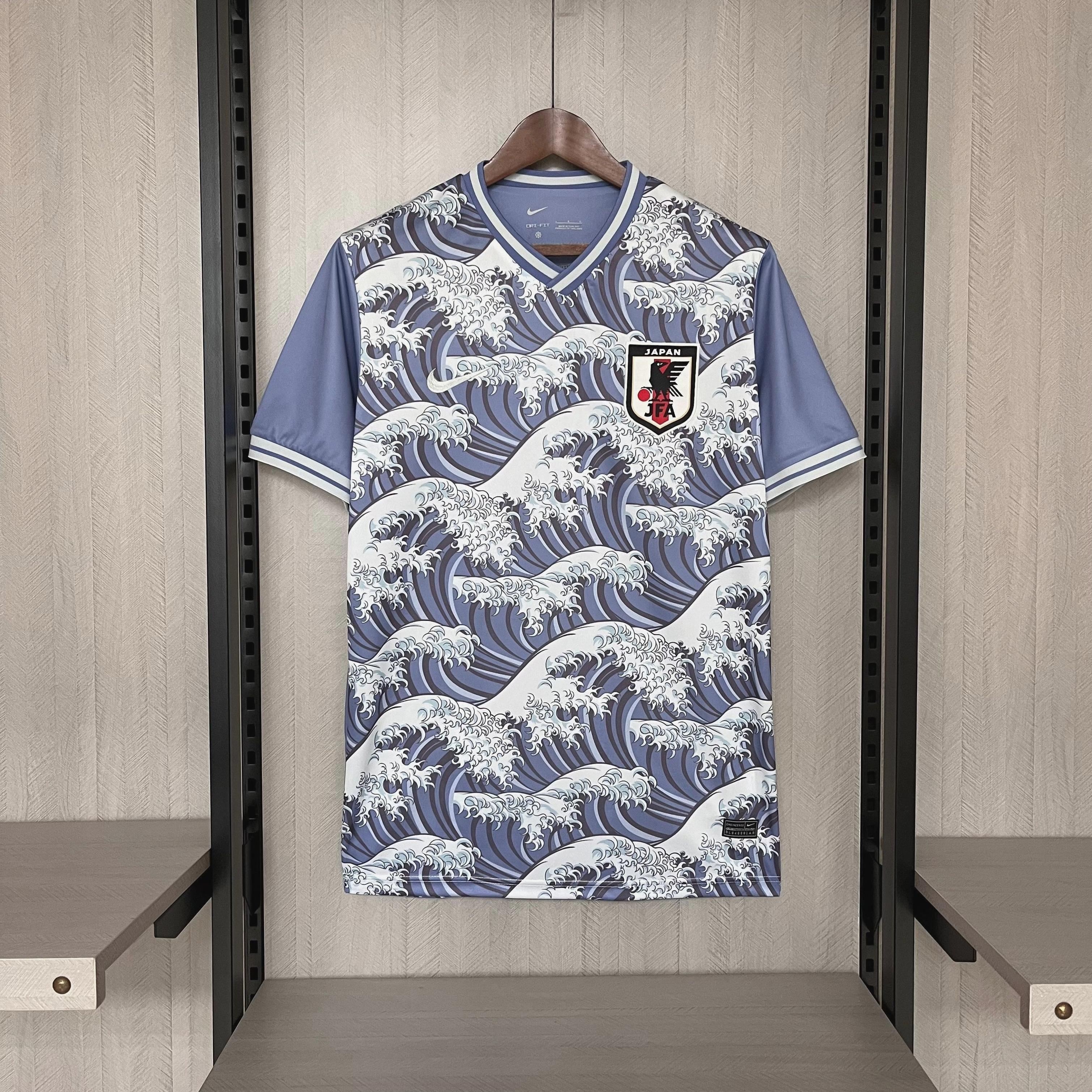 The Retro1999 Japan 2024 Special Edition football jersey, featuring a blue and white wave design inspired by Japanese art, hangs on a wooden hanger. A team crest with a black bird and red accents decorates the chest.