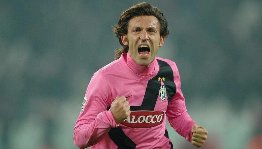 A soccer player wearing the Retro1999 Juventus 2011-12 Away Shirt in pink and black celebrates passionately on the pitch, fists clenched, mouth open, with blurred stadium lights capturing Serie A champion energy.