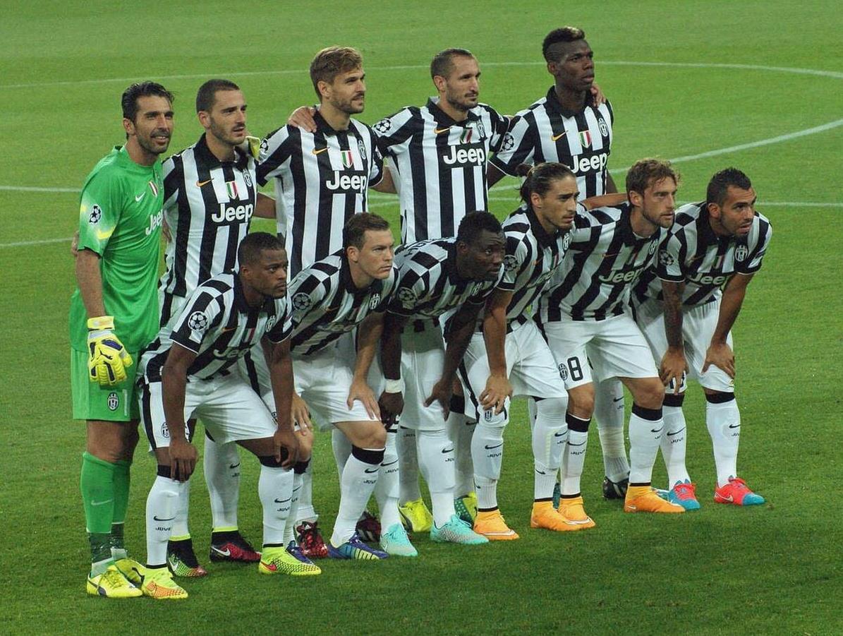 A soccer team in Retro1999s Juventus 2014-15 Home Shirt poses for a group photo on the green field before kickoff, with one player in a standout green goalkeeper kit, capturing classic Juventus nostalgia.